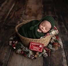 a newborn baby wrapped in a green knitted hat and sleeping in a basket with pine cones