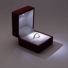 an open box with a ring inside on a white surface and light shining through it