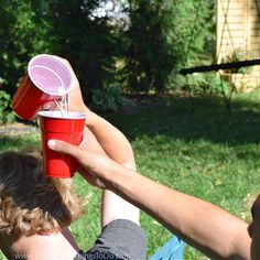 two people are sitting in the grass and one is holding a red cup with water