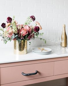 pink and gold flowers in a brass vase on a white countertop with wine glasses