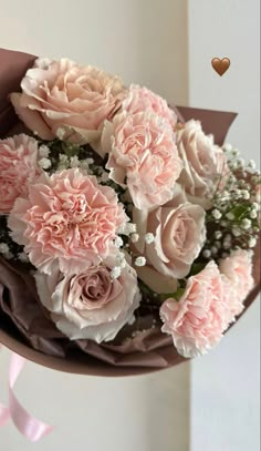 a bouquet of pink flowers with baby's breath in the background and a heart hanging from it