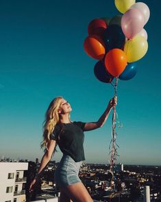 a woman is holding several balloons in the air on top of a building with cityscape in the background