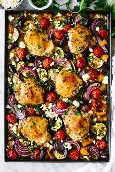 an overhead shot of chicken, tomatoes, onions and feta cheese on a baking sheet