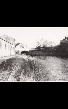 an old black and white photo of a river running under a bridge with buildings in the background