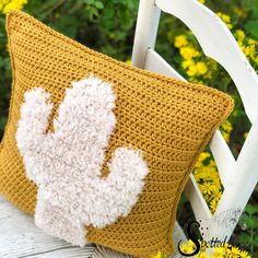 a crocheted pillow sitting on top of a white chair next to yellow flowers