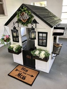 a house shaped like a dollhouse with flowers in the window boxes and welcome mat on the floor