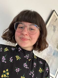 a woman wearing glasses and a black floral shirt is posing for the camera with her hand on her hips