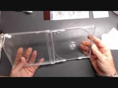 two hands holding cds in clear plastic cases on a table with papers and other office supplies