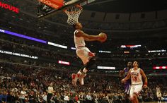 a basketball player dunks the ball in front of his opponent during a game at an arena