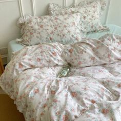 an unmade bed with white and pink flowers on the comforter, pillows and pillowcases