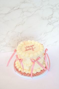 a white cake with pink ribbon on top sitting on a table next to a marble wall