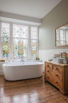 a bath tub sitting in front of a window next to a wooden dresser and mirror