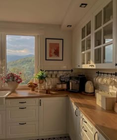 a kitchen with white cabinets and wooden counter tops next to a window overlooking the mountains