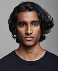 a man with long black hair is looking at the camera while wearing a black t - shirt