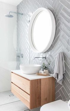 a bathroom with a round mirror above the sink and a wooden cabinet below it in front of a white tiled wall