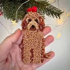 a hand holding a beaded dog ornament next to a christmas tree branch