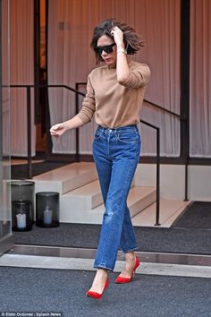 a woman walking down the street wearing high heels and a tan sweater with her hair blowing in the wind