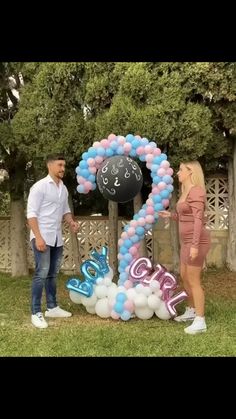 a man and woman standing in front of a balloon arch with the number twenty on it