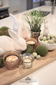 a wooden tray topped with candles and bunny figurines next to bowls filled with eggs