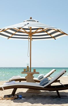 two lounge chairs under an umbrella on the beach