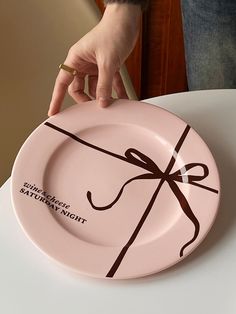 a person holding a pink plate with a brown bow on it that says, happy mother's day