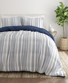 a bed with blue and white striped comforter next to a potted green plant