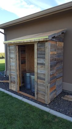 a small wooden shed sitting on top of a grass covered field next to a building