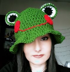 a woman wearing a green crocheted frog hat with big eyes and large ears