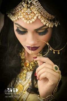 a woman with dark hair wearing a gold and red makeup looks down at her finger ring