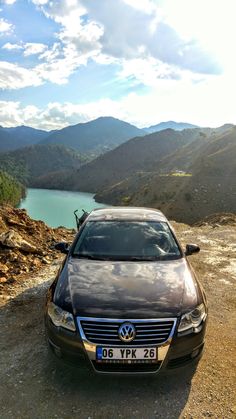 a brown car parked on top of a dirt road next to a lake and mountains