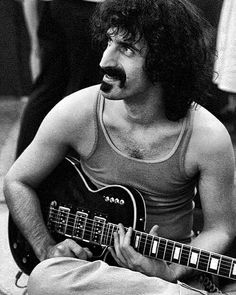 a man sitting on the ground with a guitar in his lap and moustache