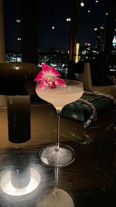 a pink flower sitting on top of a martini in a glass next to a purse