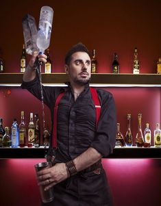 a man in an apron is holding up a plastic bottle and some bottles behind him