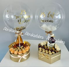 two clear balloons with gold foil lettering on them and some chocolates in a box