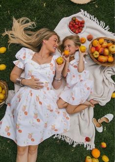 two women laying on the grass with apples and oranges