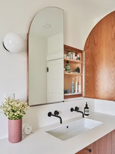 a bathroom sink sitting under a large mirror next to a wooden shelf filled with bottles