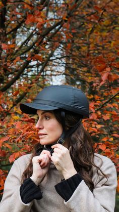 a woman wearing a black helmet standing in front of trees with orange and red leaves