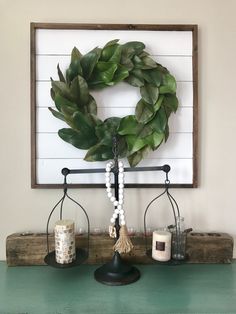 a green table with a wreath on top of it and candles in front of the frame