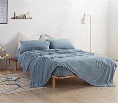 a bed with blue sheets and pillows in a white room next to a wooden floor