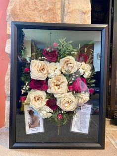 an arrangement of flowers is displayed in a shadow box on the ground next to a brick wall