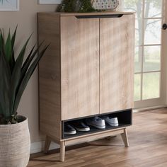 a wooden cabinet with two pairs of shoes on it next to a potted plant