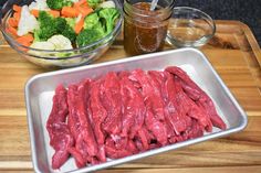 raw meat and vegetables on a cutting board next to a bowl of broccoli