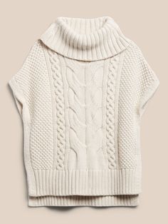 a white sweater with cable knits on the shoulders and collar, in front of a beige background