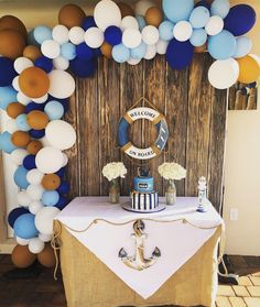 a table topped with a cake covered in blue, white and gold balloons next to a wooden wall