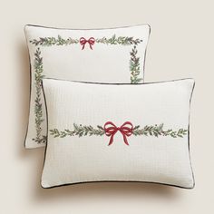 two white pillows with red bows and green leaves on the front one has a bow