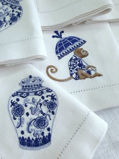 embroidered napkins with monkey holding an umbrella and blue chinese vase on white linen background