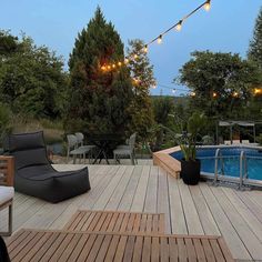 an outdoor deck with lounge chairs, lights and a pool in the background at dusk