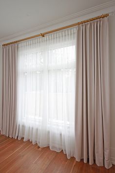 an empty room with white curtains and wood floors