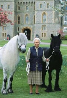 an older woman standing next to two black and white horses in front of a castle