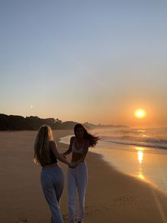 two women walking on the beach at sunset with one holding the other's hand